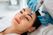 A woman receiving a facial treatment with a modern skincare device, lying on a spa bed with a beautician wearing gloves attending to her.