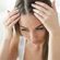 A person with long hair is looking down while parting their hair to reveal the scalp with their hands. The image focuses on the top of their head and hands.