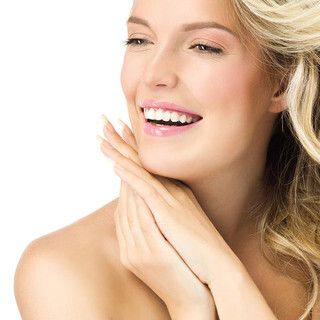 A person with long, wavy blonde hair, smiles brightly while looking slightly to the side. They have pink lips, rosy cheeks, and are resting their chin on their hands. The background is plain white, emphasizing their radiant complexion and happy expression.