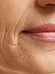 Close-up image showing the lower half of a person's face with visible wrinkles around the mouth, focusing on the textured skin and the lips that are lightly colored with lipstick. The image highlights the details of aging skin.