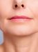 Close-up of a mature woman's lower face showing her lips and chin against a gray background, emphasizing healthy skin and subtle makeup.