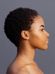 Profile of a person with short, curly hair, viewed against a plain grey background. They have a serene expression on their face and their smooth skin is highlighted by the lighting, which accentuates their facial features.