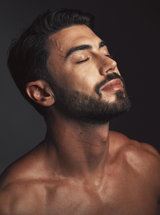 man with beautiful skin looks up and to the side with dramatic lighting against a dark background
