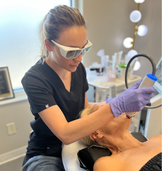 A skincare professional using a handheld device on a relaxed female client's face during a facial treatment in a modern clinic.
