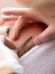 A close-up of a person receiving a professional facial treatment. A gloved hand holds a small scalpel, gently scraping the person's cheek. The individual has their eyes closed and appears relaxed while lying down on a white towel.